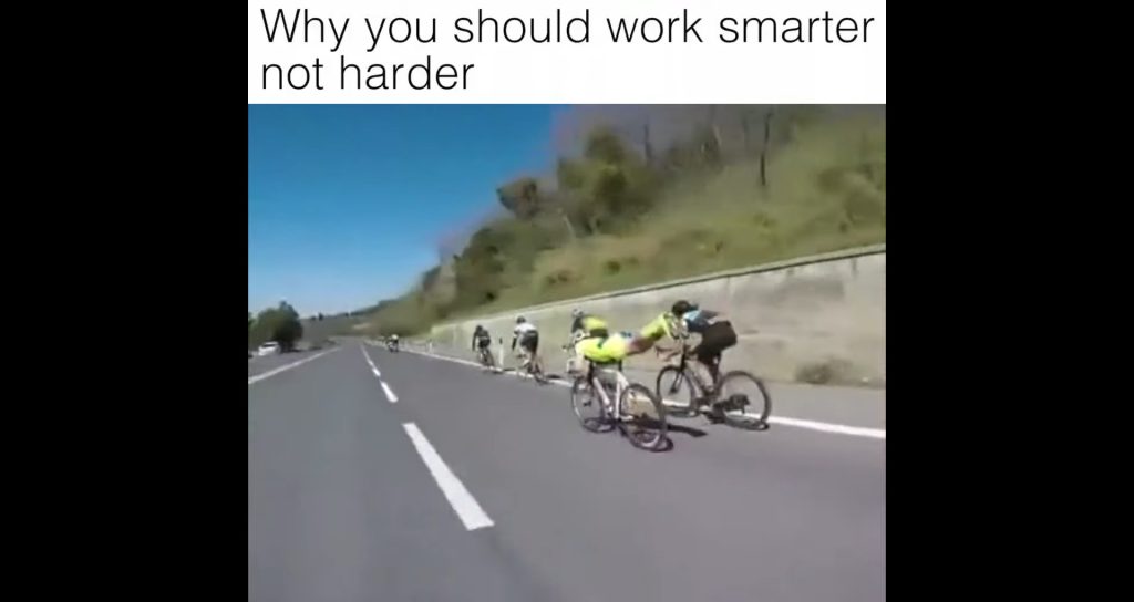 A group of cyclists pedal uphill on a road, while one cyclist in yellow rides effortlessly by holding onto a moving car. Text at the top reads, Why you should work smarter not harder—just like an SDVOSB engineering expert.
