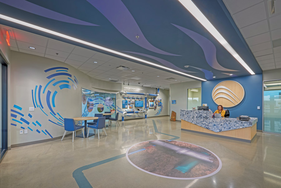 Modern reception area with ocean-themed decor, wave patterns, circular floor graphic, display screens, and a receptionist at a blue-patterned desk—reflecting the innovative touch of a whitewater engineer.