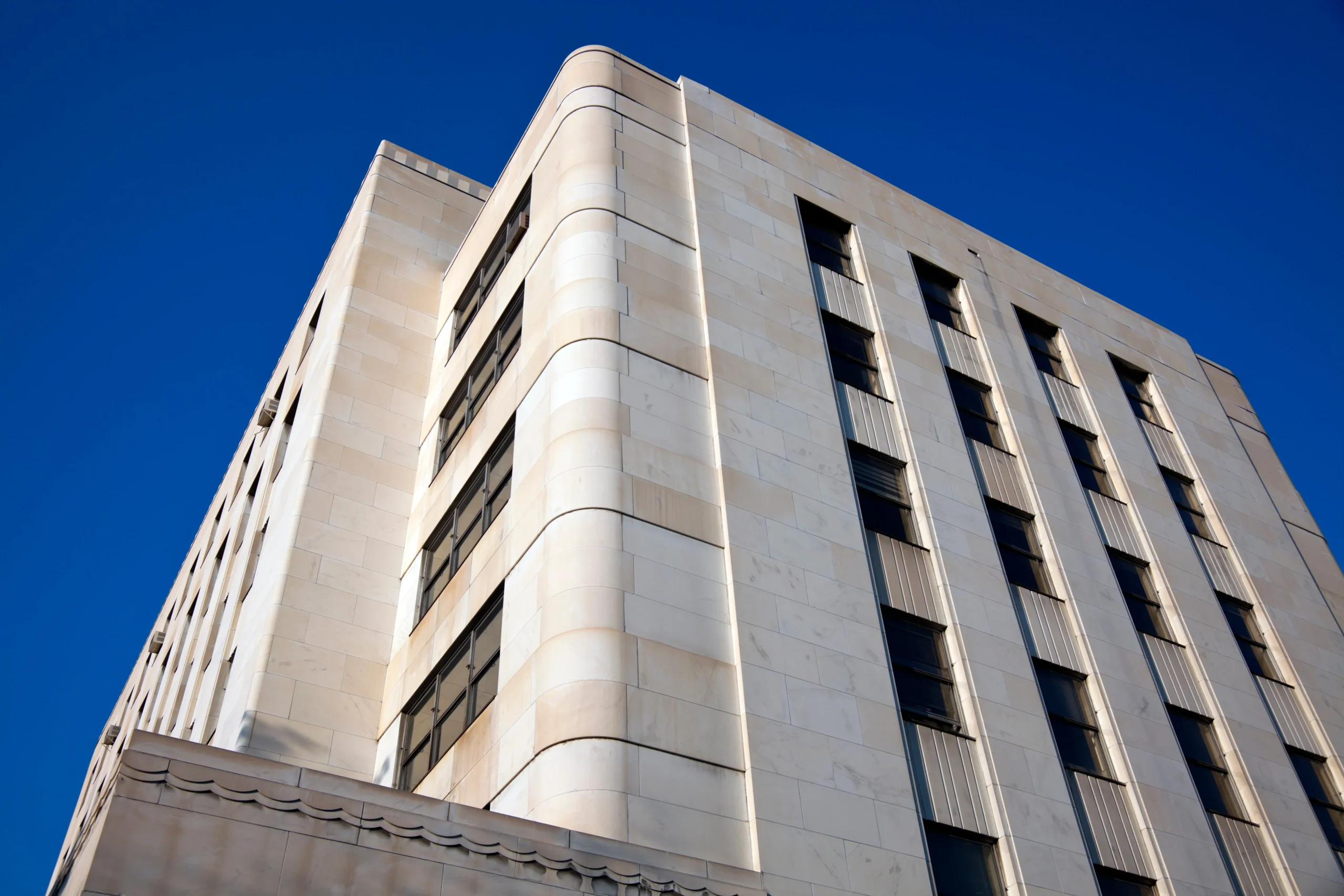 A low-angle view of a white Art Deco building with curved corners, vertical windows, and a smooth stone facade against a clear blue sky—an inspiring example for any structural engineer or Denver engineer.