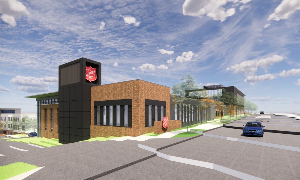 A modern Salvation Army building with brick and black paneling, reflecting thoughtful civil engineering, sits on a sloped street under a partly cloudy sky. A blue car is parked nearby, and trees line the landscape around the building.