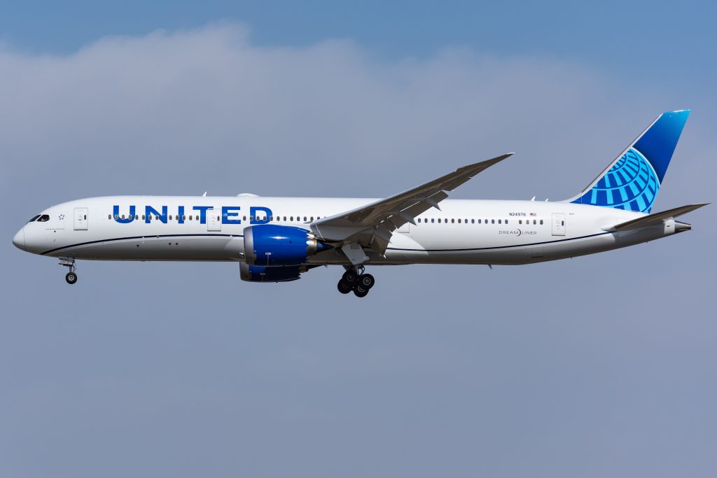A United Airlines Boeing 787 Dreamliner airplane in flight against a blue sky with some clouds, highlighting the airline’s name and blue globe logo—an inspiring sight for any structural engineer or SDVOSB engineering professional.