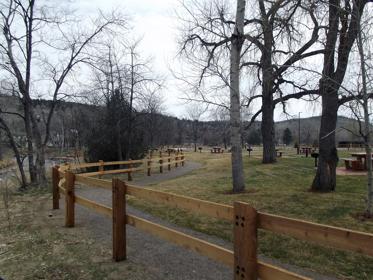A winding gravel path bordered by a wooden fence runs through a grassy park area with tall, leafless trees—an inviting scene that could inspire any Colorado engineering or structural engineer seeking peace and fresh ideas. The sky is overcast.