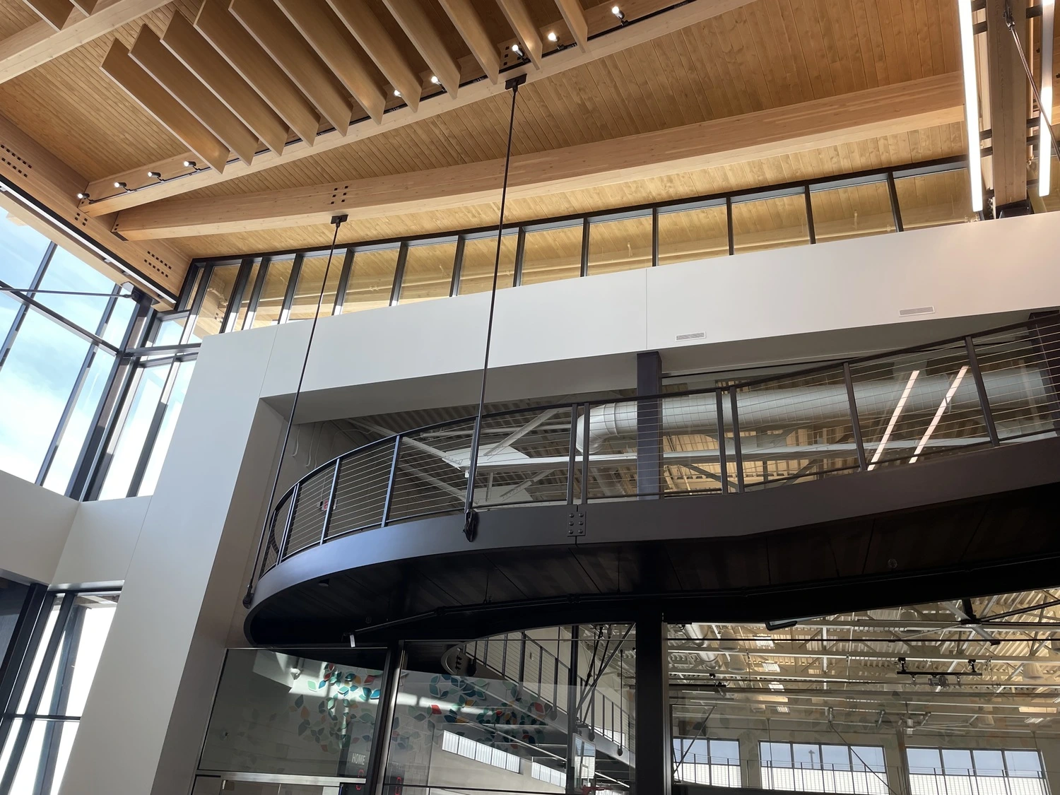 Modern interior with large windows, wood ceiling beams, and an upper-level glass-walled balcony with black railings—showcasing architectural expertise inspired by a Denver engineer. Natural light highlights the thoughtful civil engineering design.