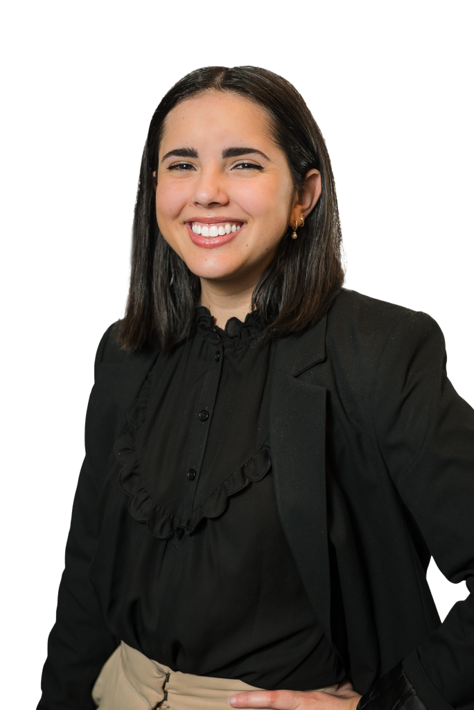 A young woman with shoulder-length dark hair, wearing a black blouse with ruffles and a black blazer, smiles confidently at the camera with one hand on her hip—showcasing the poise of a talented structural engineer.