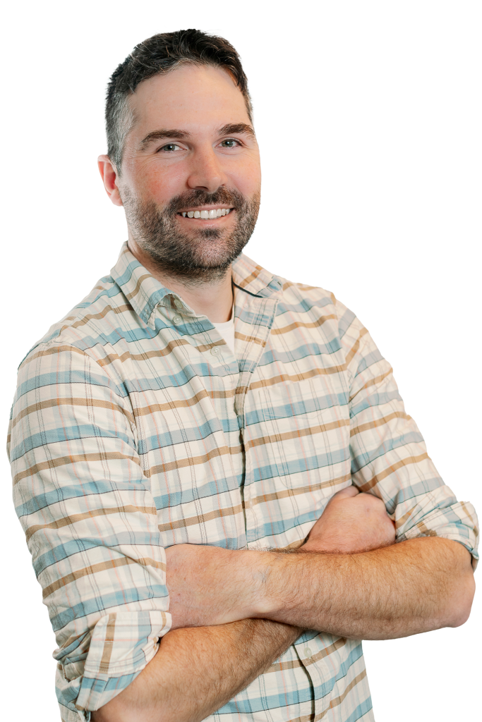 A Denver structural engineer with short dark hair and a beard, wearing a light plaid shirt, smiles with his arms crossed in front of him against a white background.