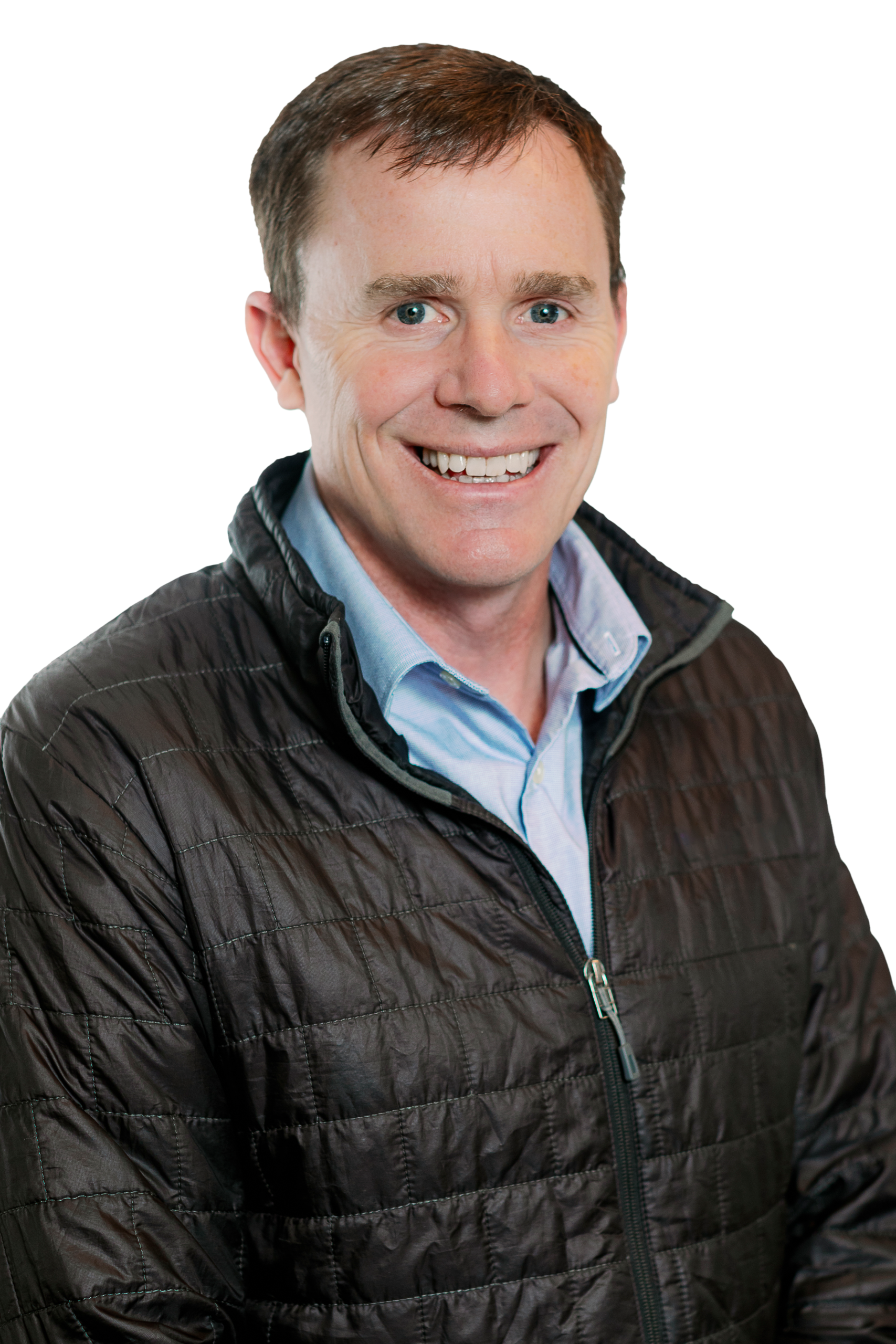 A smiling man with short brown hair, a structural engineer, wears a dark quilted jacket over a light blue collared shirt. The background is transparent.