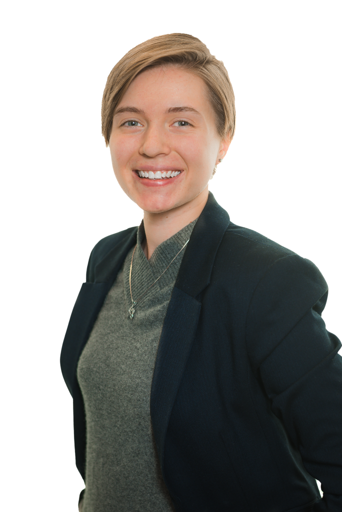 A person with short light brown hair wearing a dark blazer over a gray top smiles at the camera against a white background, embodying the professionalism of a Denver engineer.
