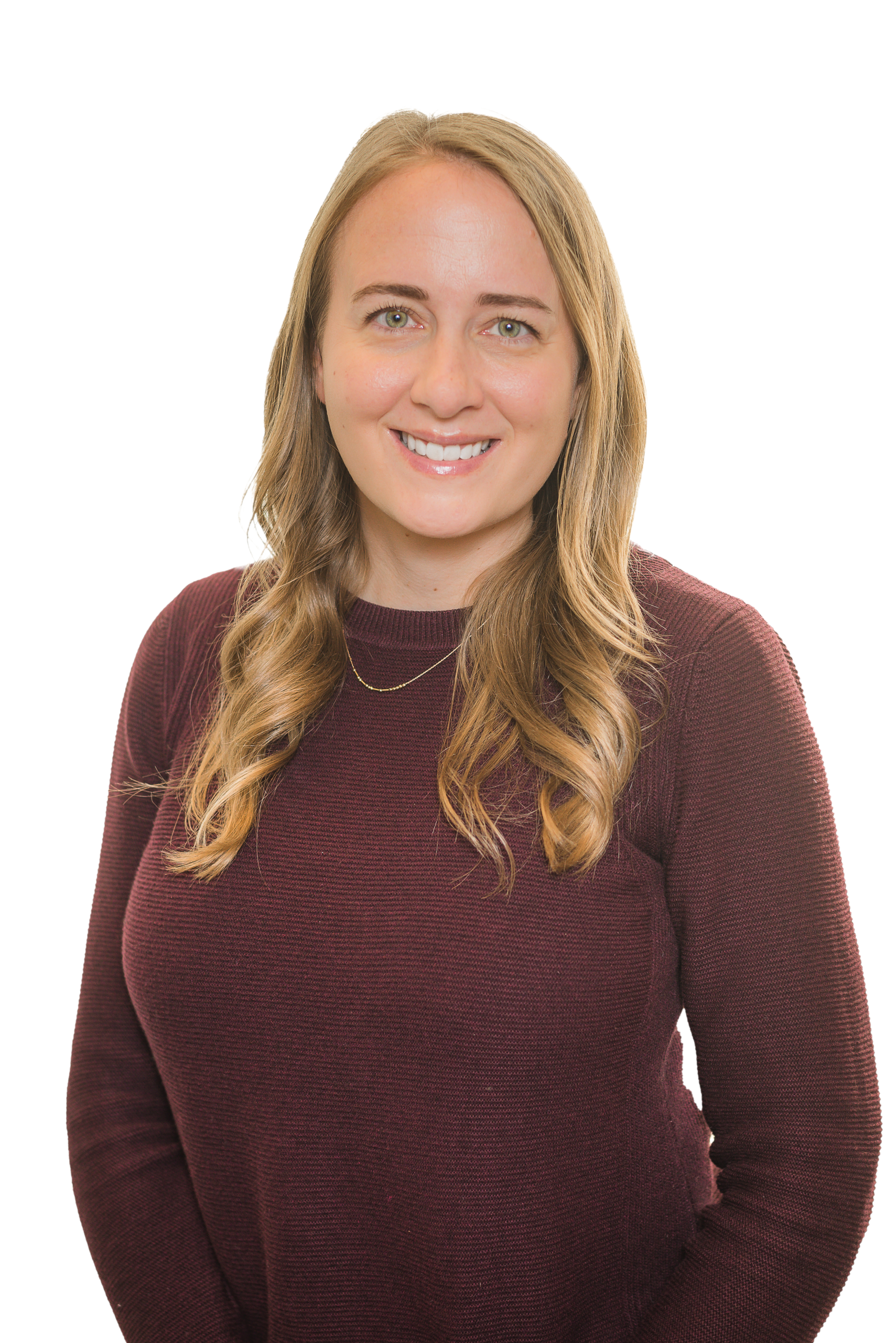 A woman with long, wavy blonde hair is smiling. She is wearing a maroon sweater and a delicate necklace, standing against a plain black background—an inspiring Denver engineer ready to make a difference.
