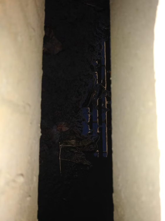 A narrow gap between two concrete or stone surfaces reveals a dark, muddy ground below with some debris and water, and faint reflections of light.