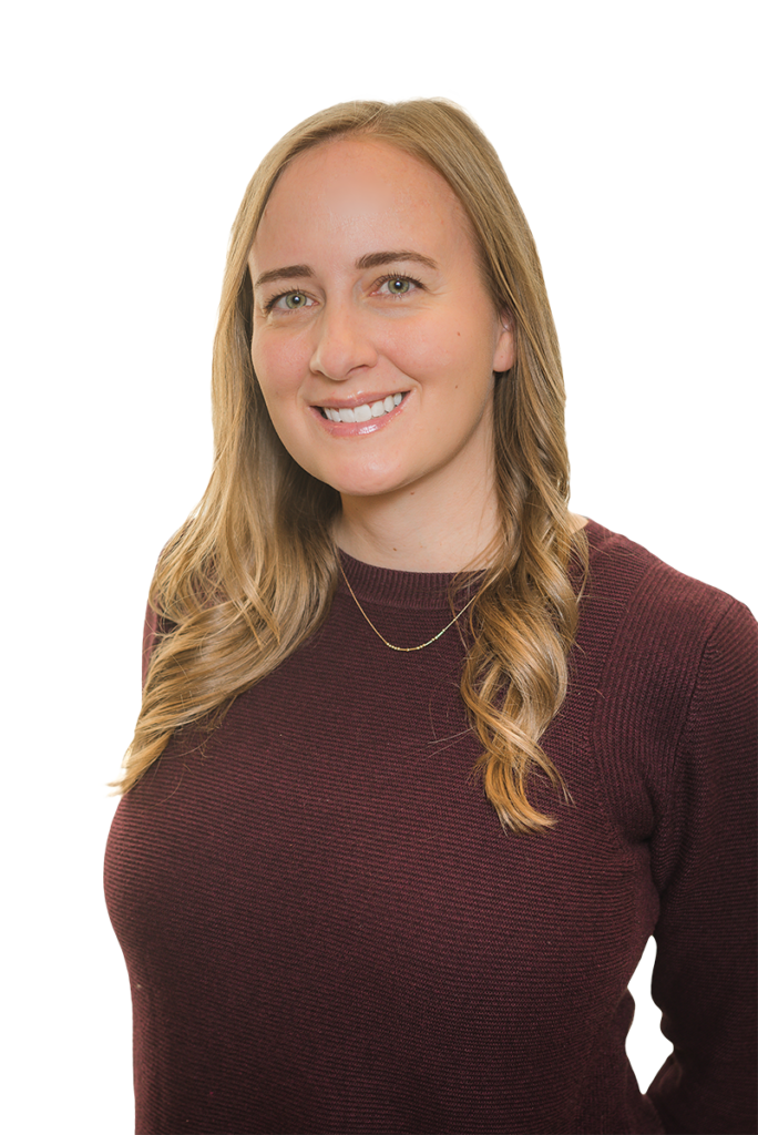 A woman with long, wavy blonde hair wearing a maroon sweater and a gold necklace smiles at the camera against a plain white background.